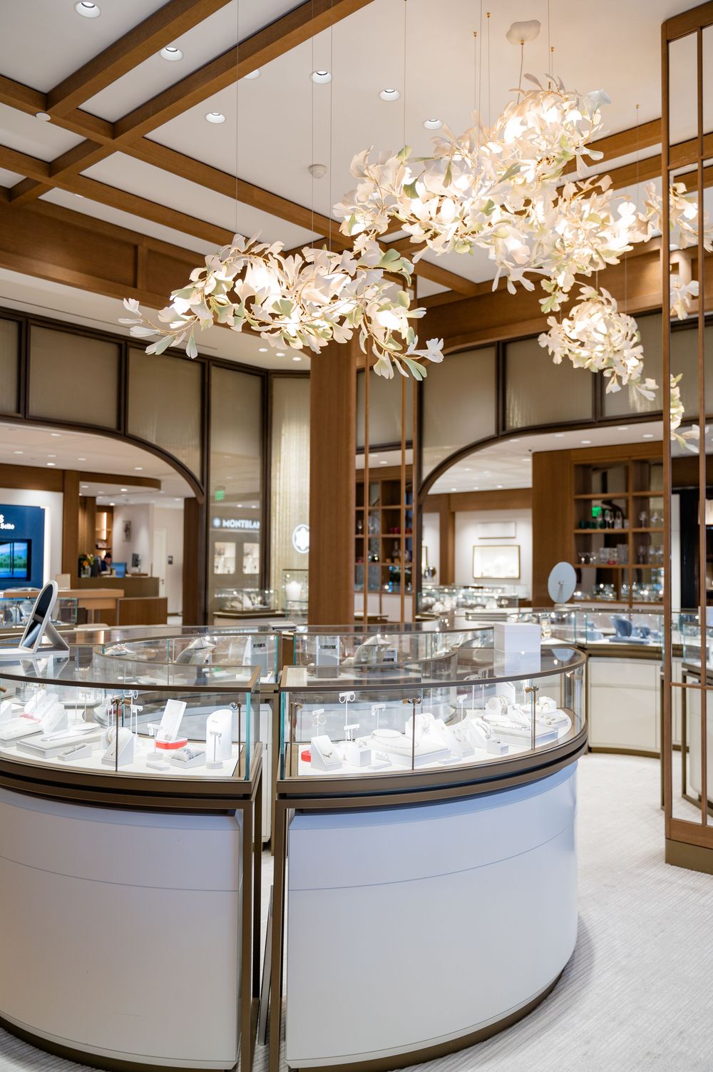 Luxury jewelry store interior with curved glass display cases and elegant white cherry blossom light fixtures.