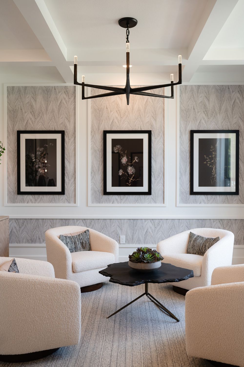 Modern living room with white curved sofa, black chandelier, and gray wallpaper features three framed artworks on the wall.
