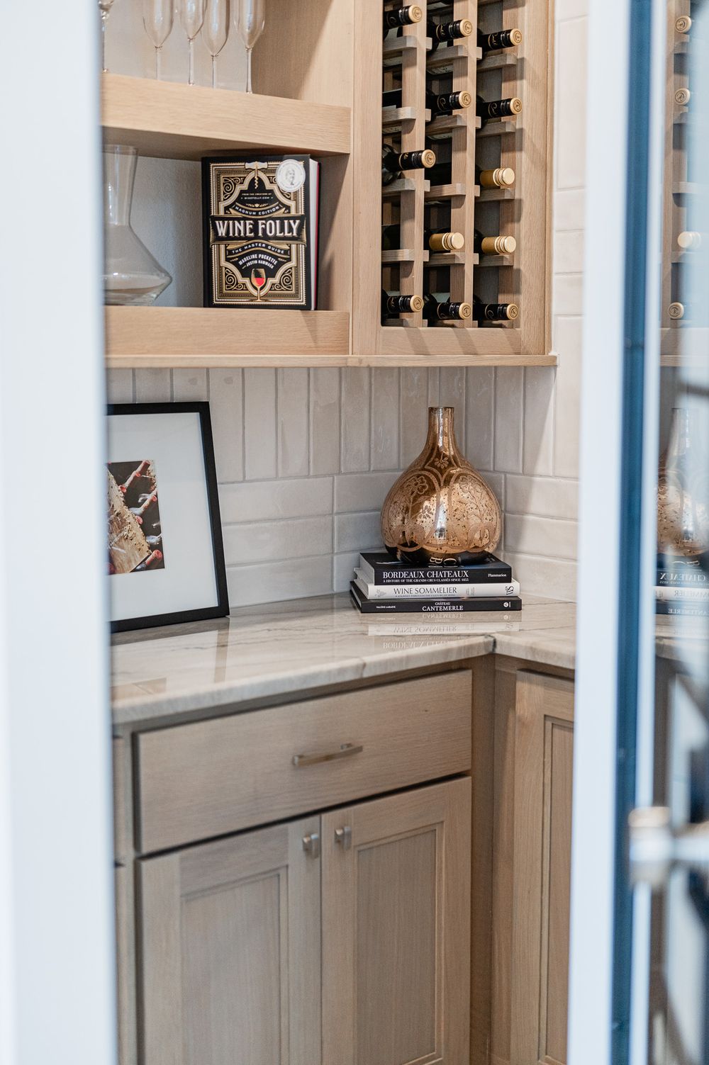 Modern wine storage area with built-in wooden rack, white cabinets, marble countertop, and decorative wine-themed decor.