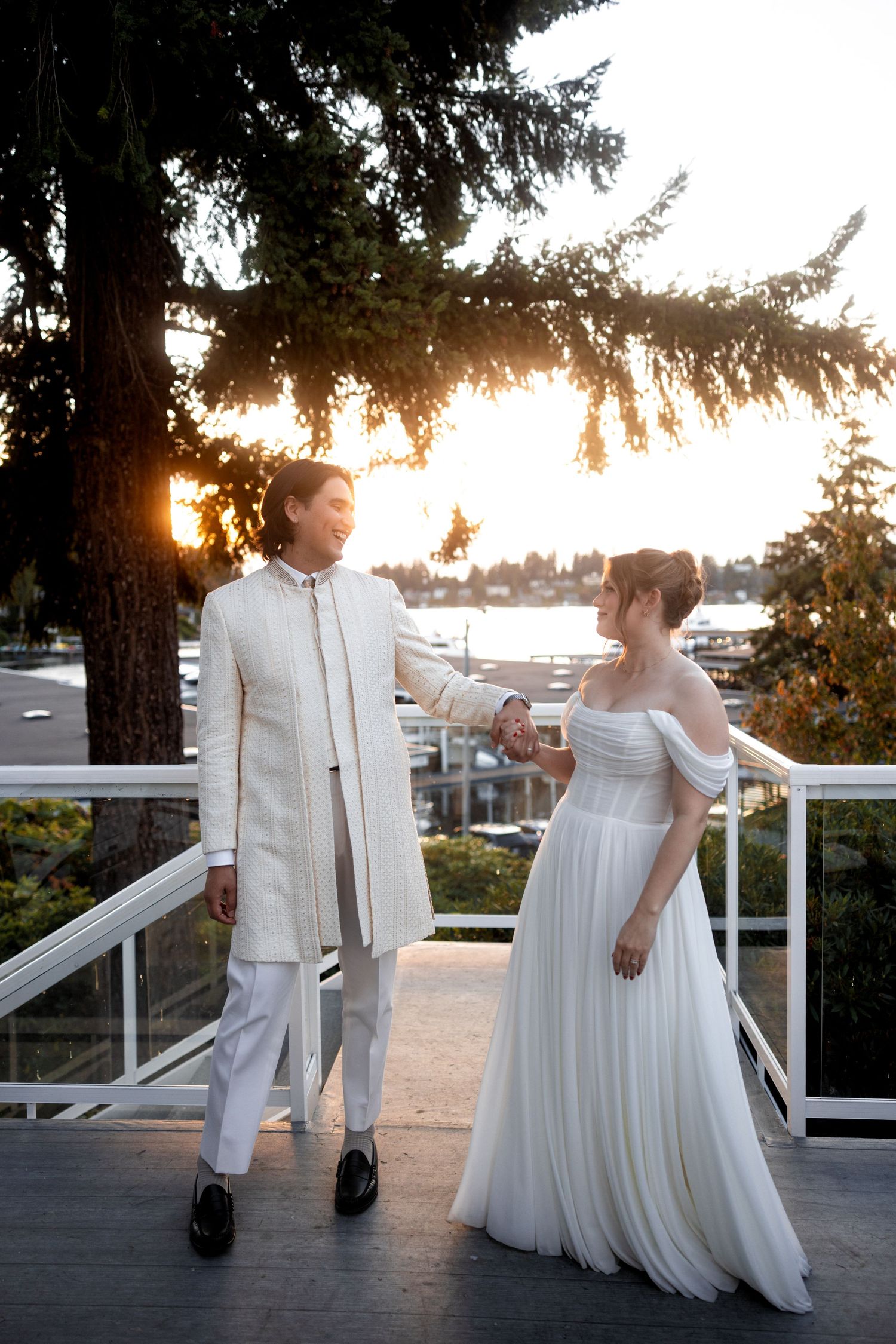 A couple poses on a white deck railing at sunset with water views in the background.