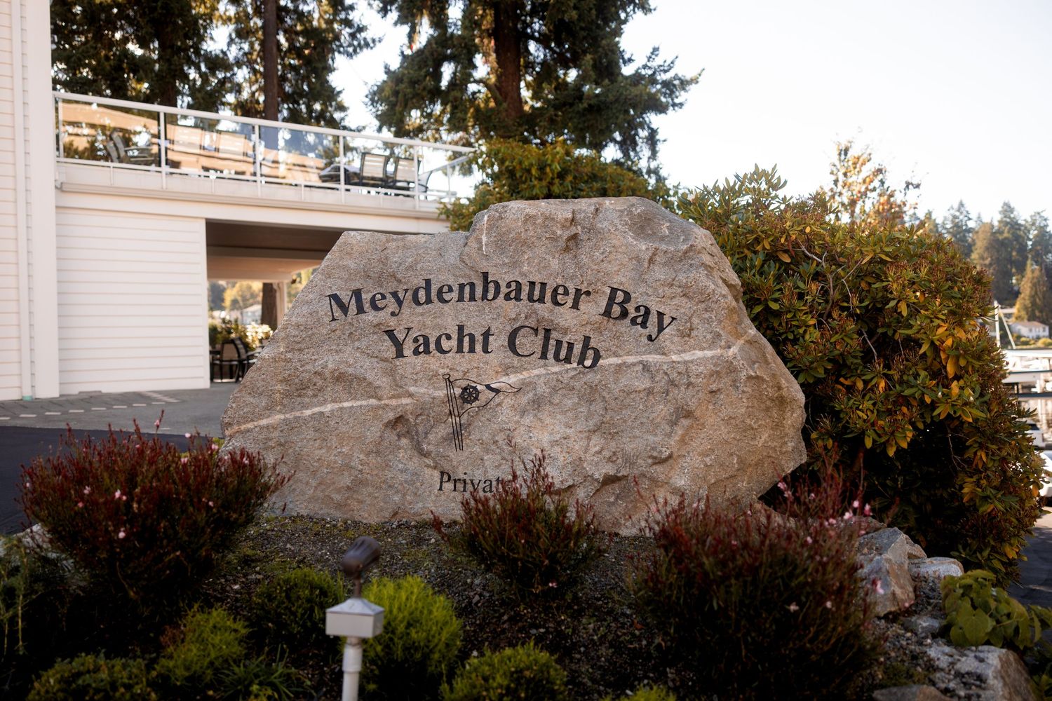 Large stone sign for Meydenbauer Bay Yacht Club nestled among trees and landscaping.