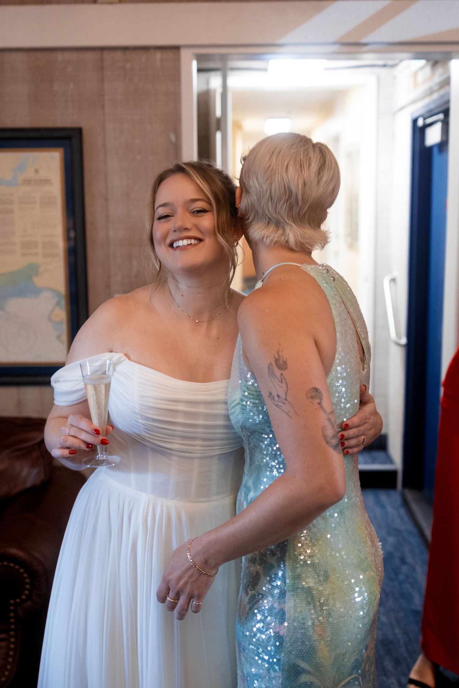 A heartwarming moment between two wedding guests sharing laughter in an indoor hallway.