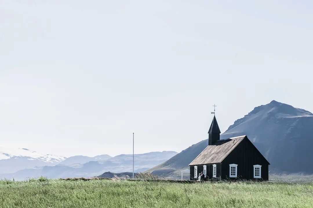 Small black wooden church set against open fields and Icelandic mountains.