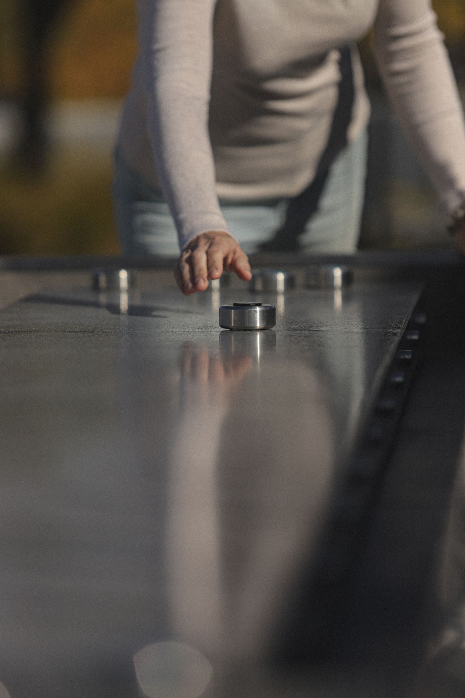 Hands reaching across a reflective surface to arrange metallic objects in a sequential pattern.
