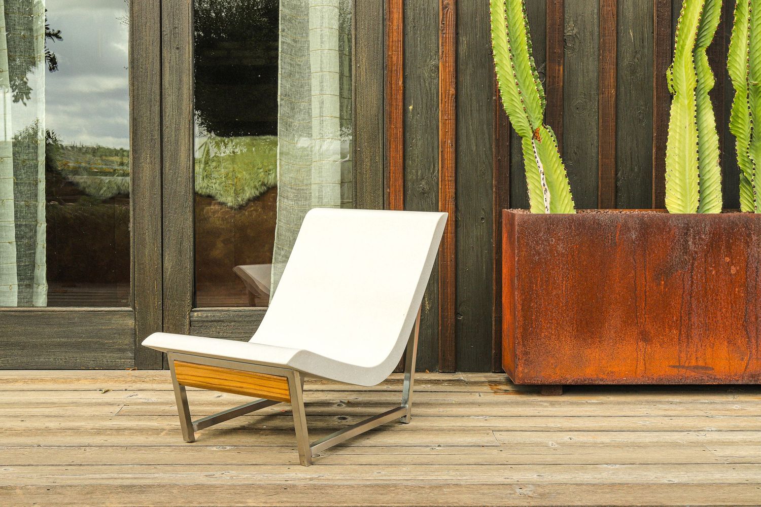 Modern outdoor patio furniture with sleek metal frames and white cushions arranged on a wooden deck.