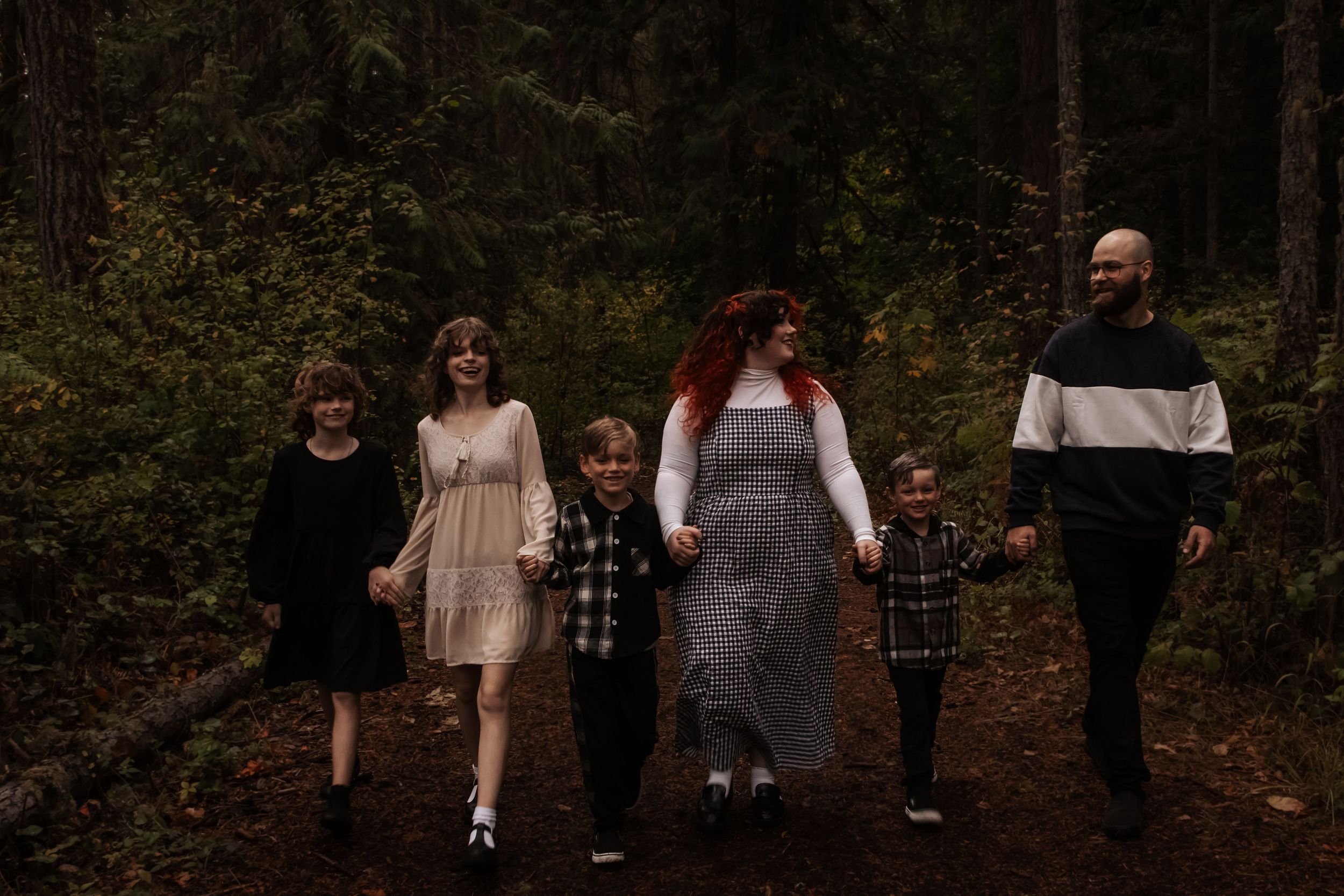 Family of six walking hand in hand through a dark moody forest on an autumn day.