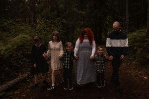 Blended family with four children and parents holding hands walking through a lush green forest.