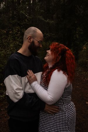 Couple gazing at each other lovingly on a dark forest path in casual attire.