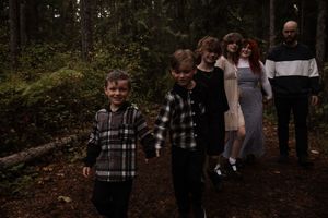 Family walking through a dense forest path in casual autumn attire.