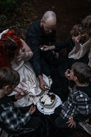 Family gathered in a forest sharing a black and white layered celebration cake.