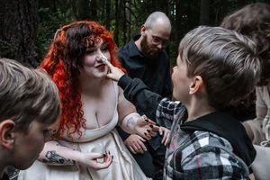 Child touching a red-haired womans face during an outdoor forest family session.