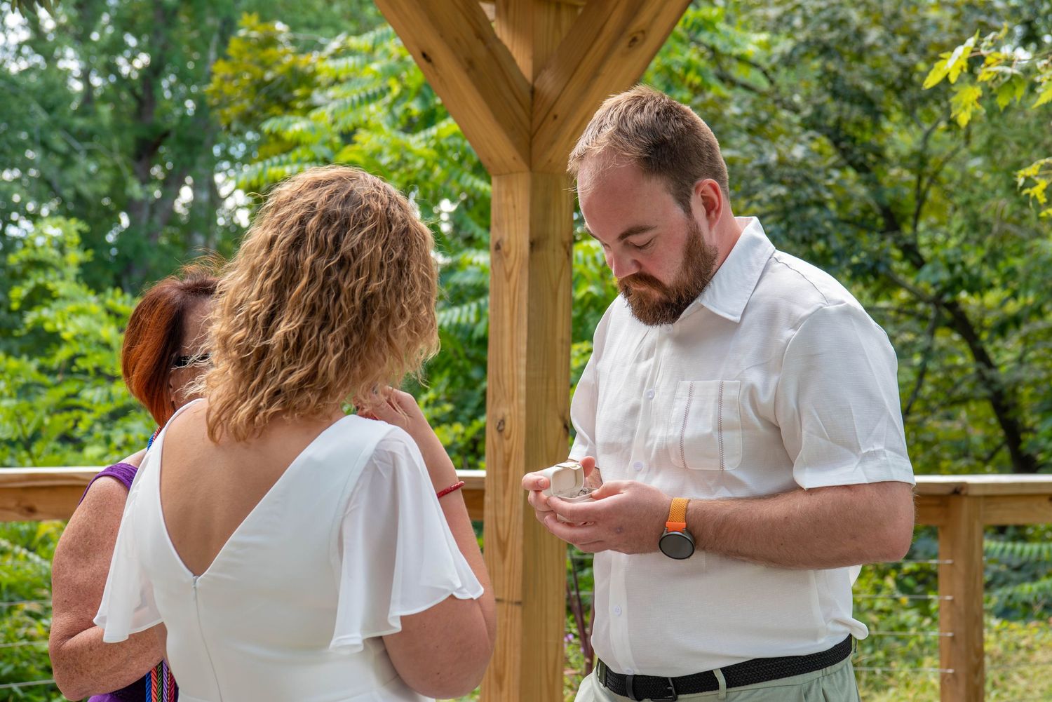 A handfasting ceremony ritual being performed outdoors under a wooden gazebo with colorful ribbons.