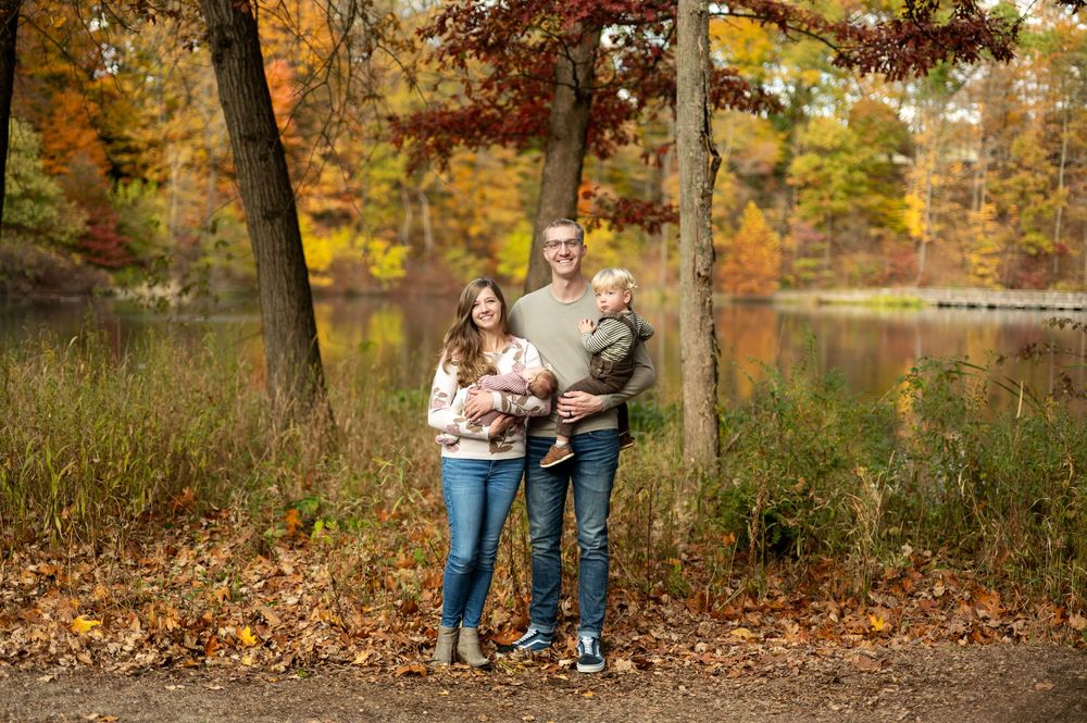 Happy family of four posing together in a colorful fall forest setting near a reflective lake.