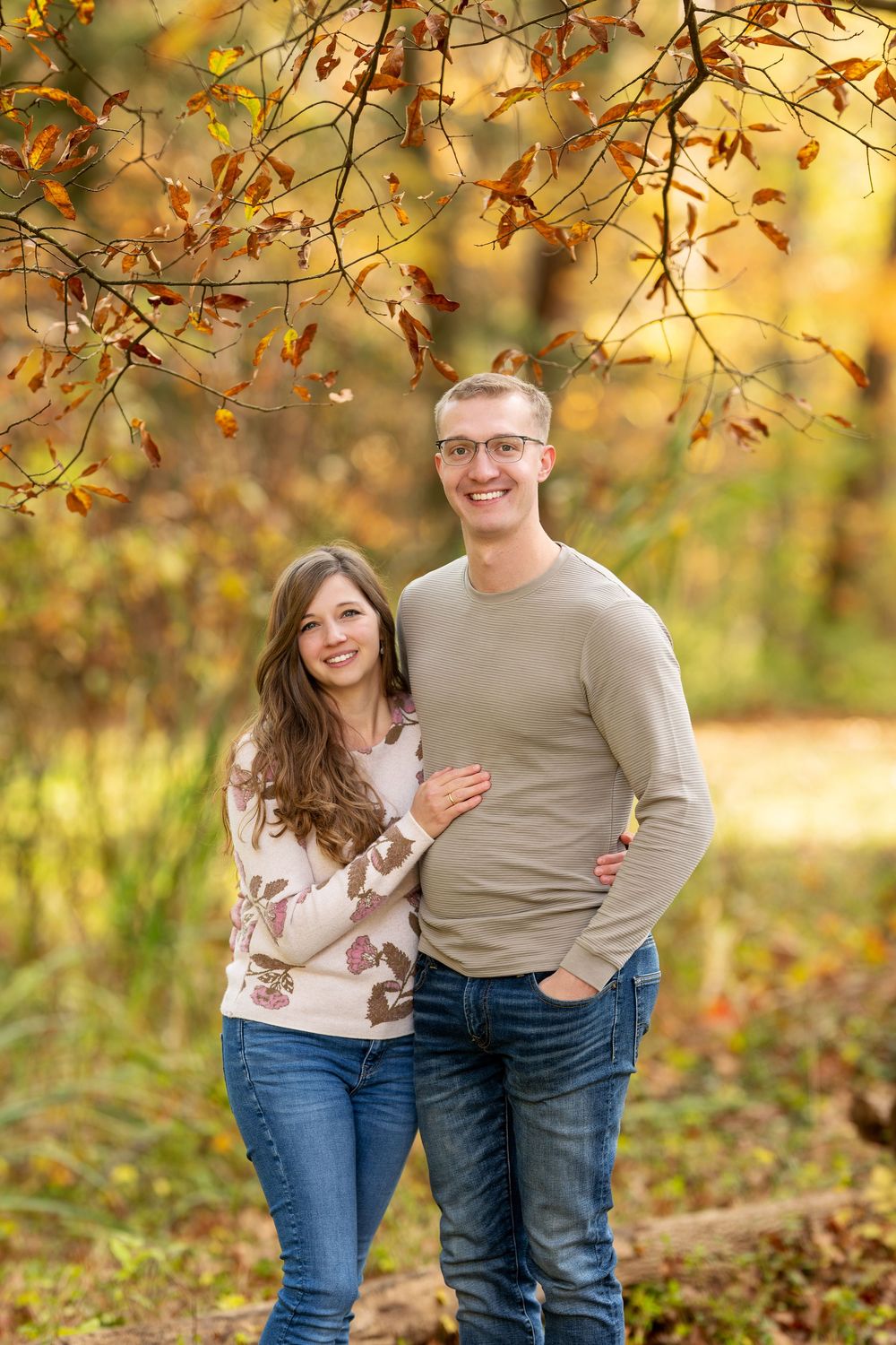 A smiling young couple poses together under autumn foliage in a forest park.