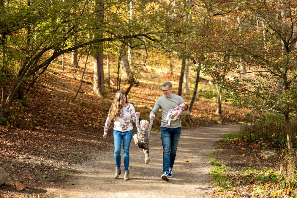 A joyful family runs together along a sunny autumn forest path with their child.