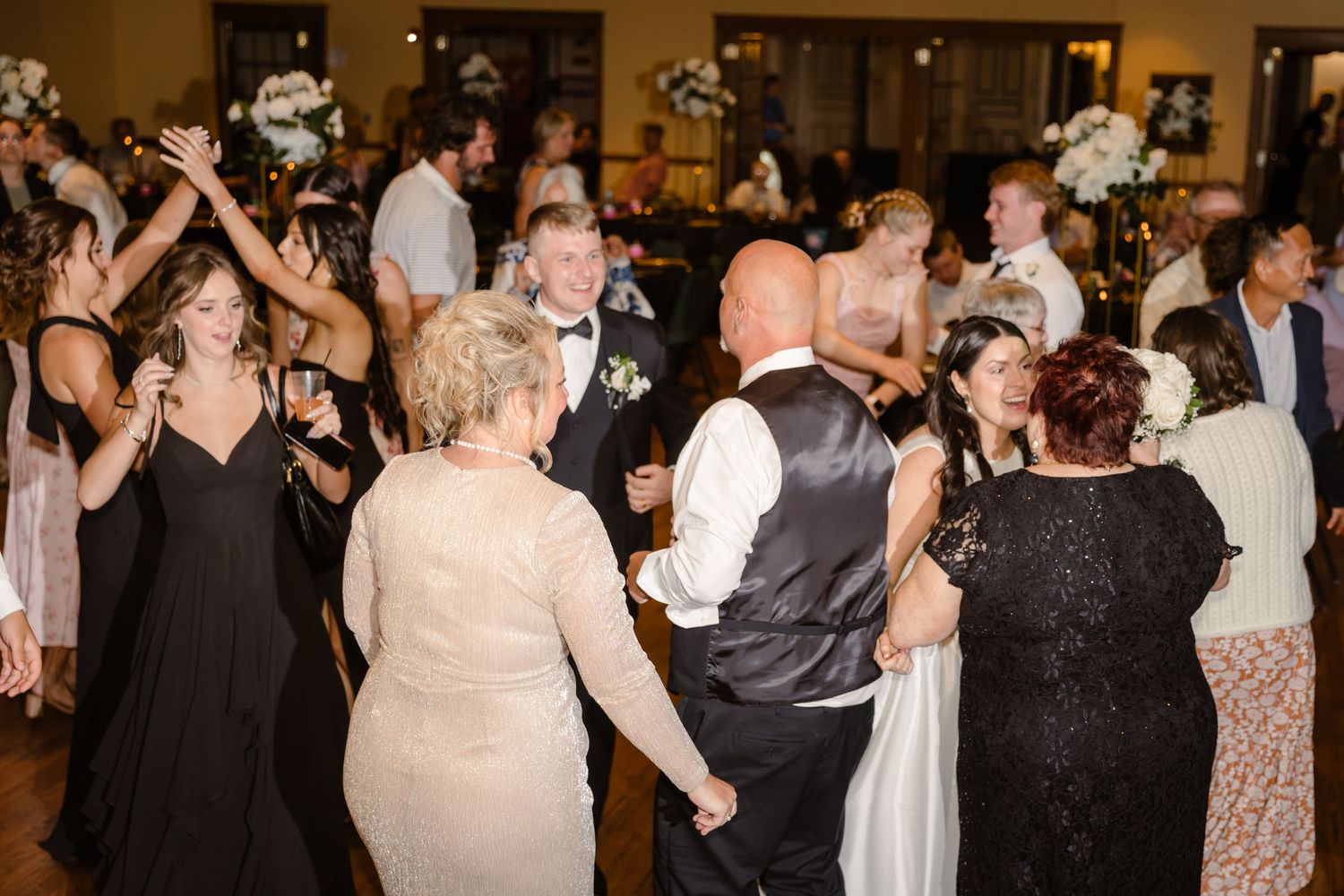 A lively wedding reception dance floor filled with guests in formal attire dancing and celebrating together.