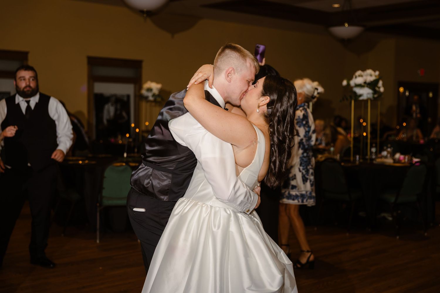 A couple shares a romantic dance at their wedding reception in a warmly lit ballroom.