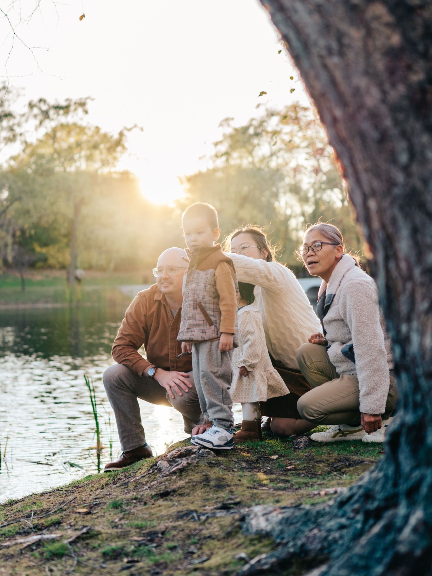 Boston family photographer captures grandparents and toddler exploring pond at golden hour in Brookline MA