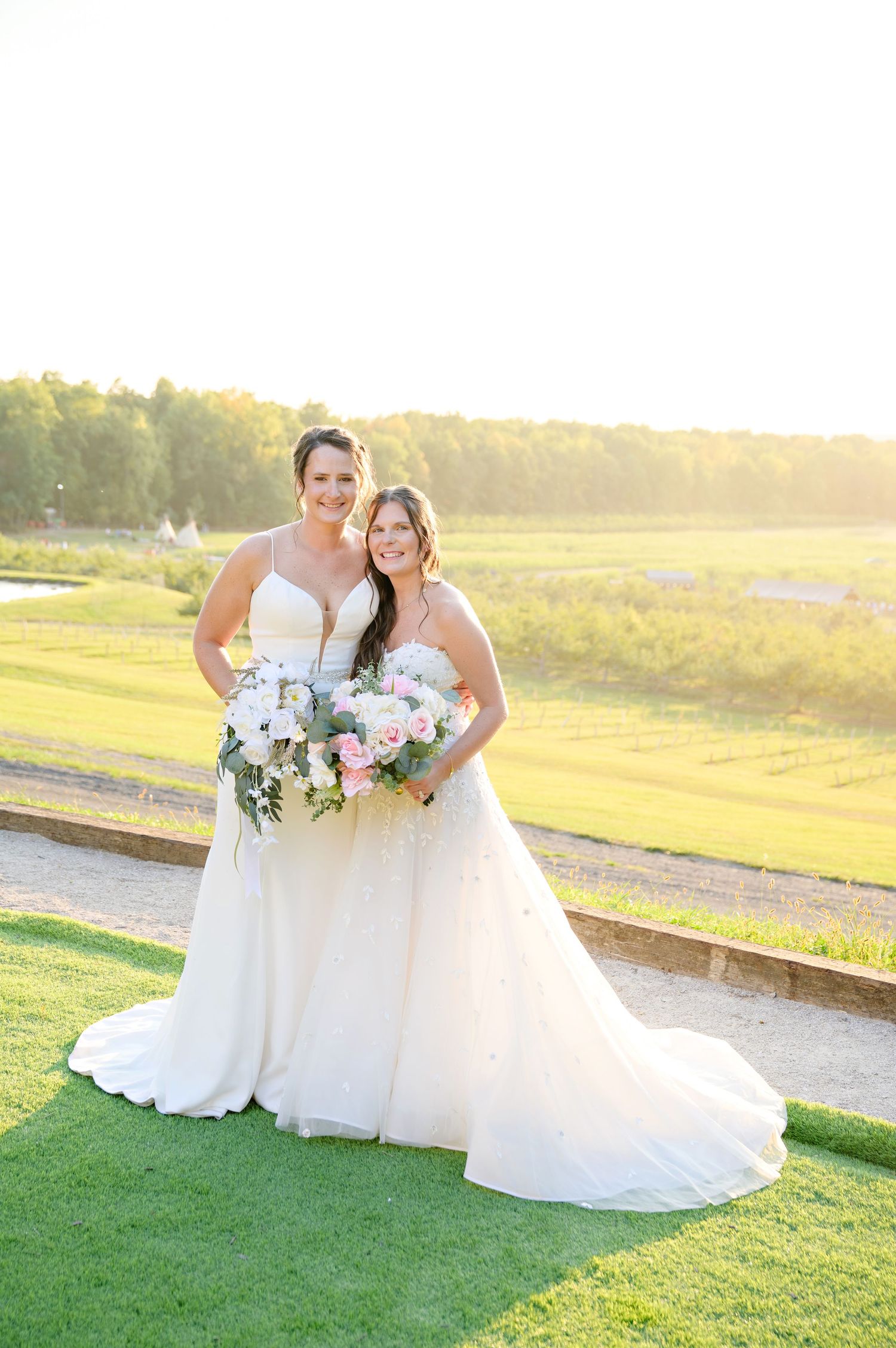 Two brides pose in white wedding dresses while holding floral bouquets at golden hour at Mapleside Farms in Brunswick Ohio in September