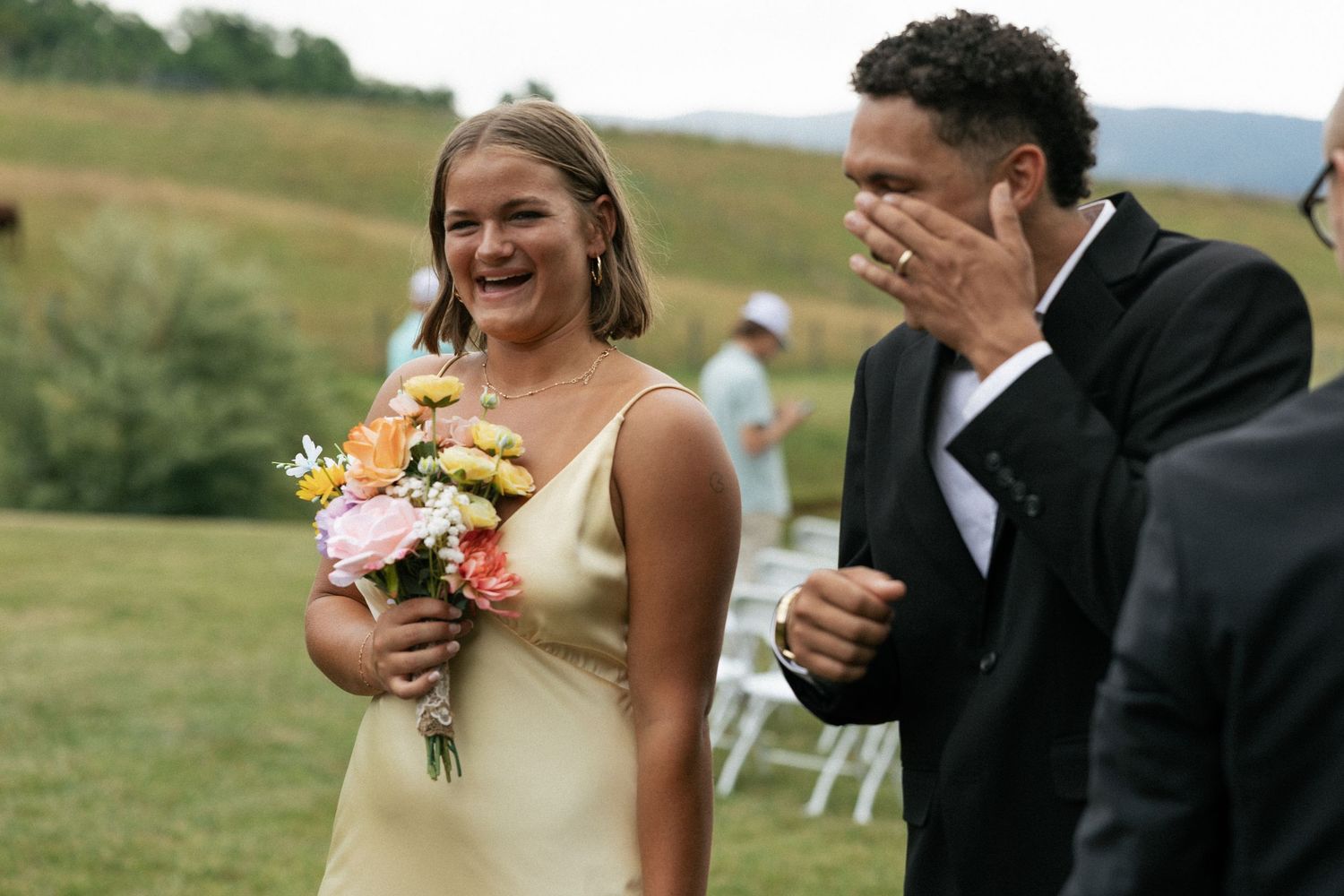 A joyful couple shares a candid moment together during their outdoor wedding ceremony in a scenic field.