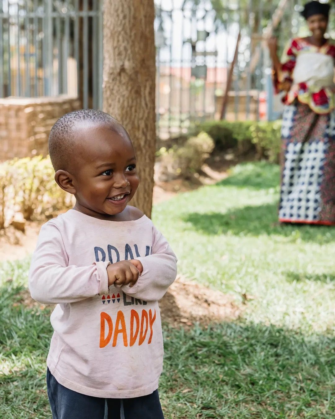 Young boy stands outside holding a “I love my daddy” sign, smiling in a playful family moment.