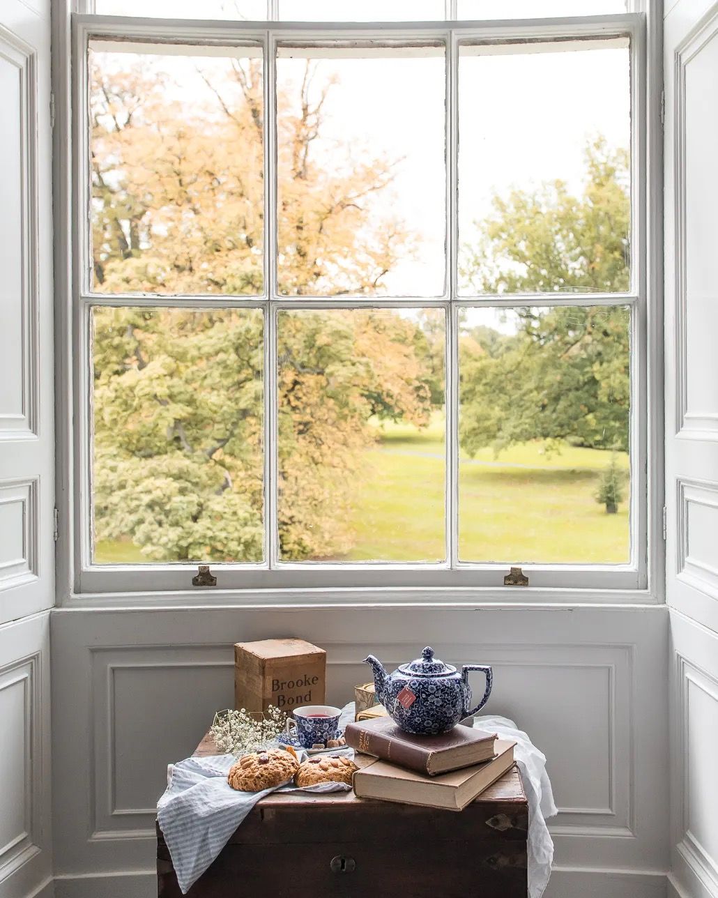 A breakfast table set beside a large window overlooking a sunny garden.