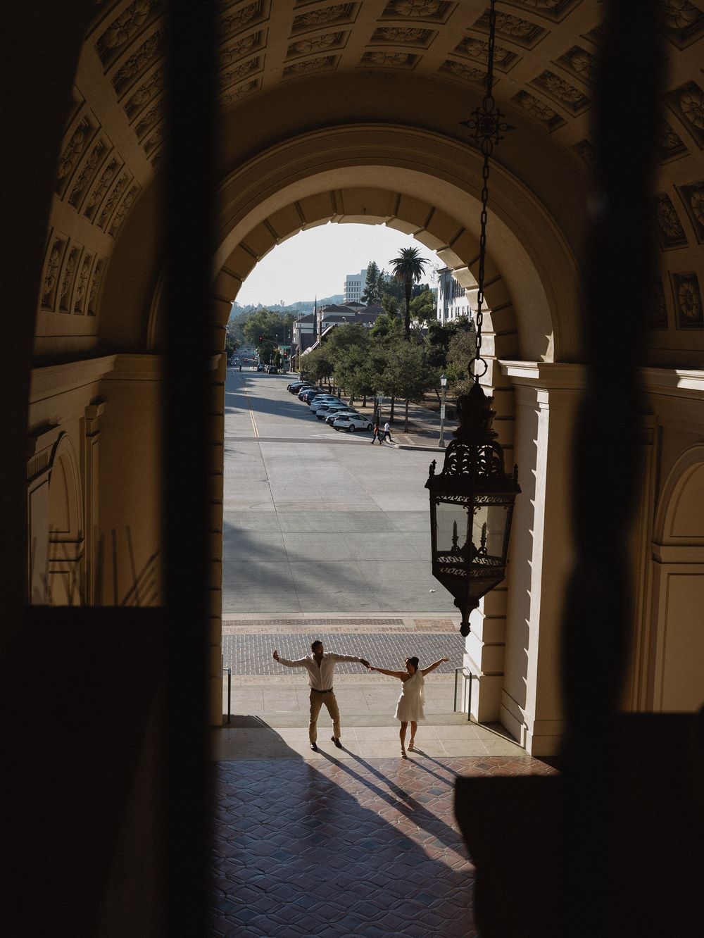 Playful couple dancing under the dome of Pasadena City Hall in cinematic golden light.