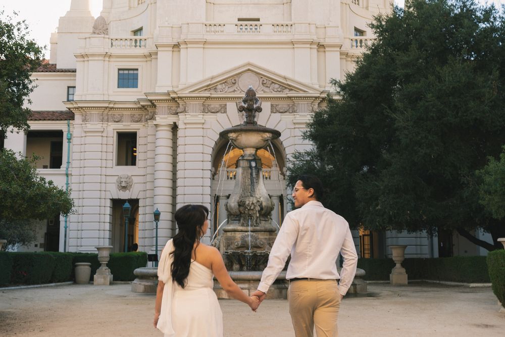 Couple walking hand in hand through Pasadena City Hall courtyard during engagement session.
