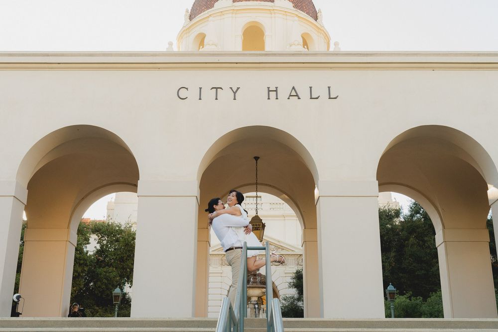 Couple hug together at sunset, holding hands in Pasadena City Hall plaza.