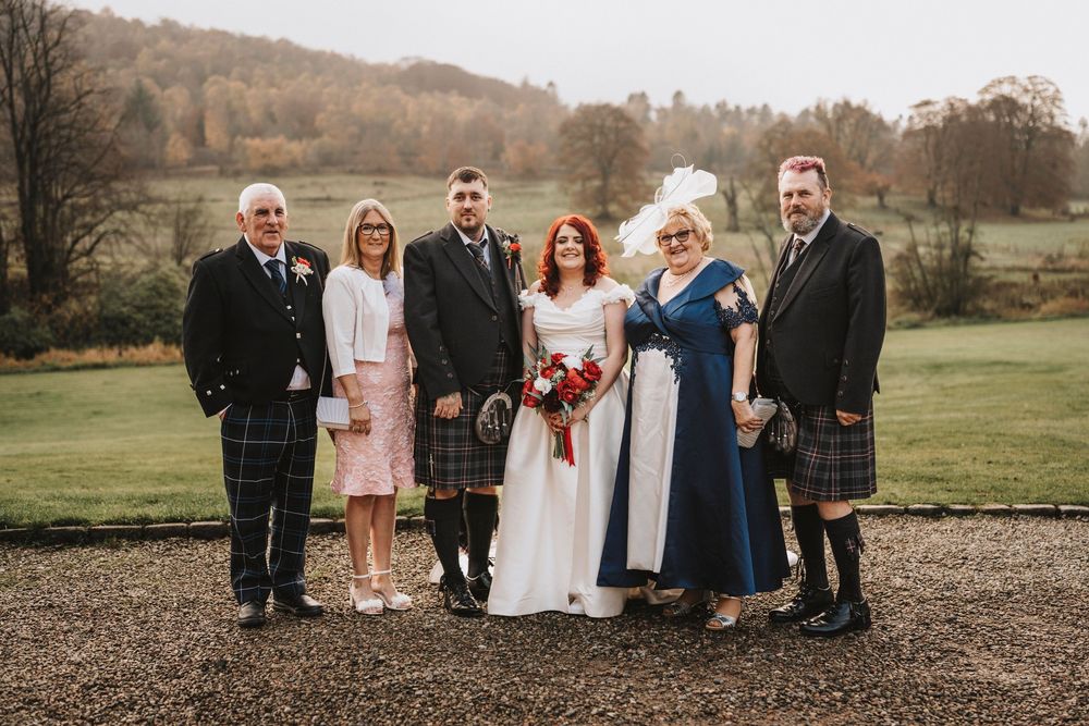 Wedding party poses for group photo outdoors in formal attire.