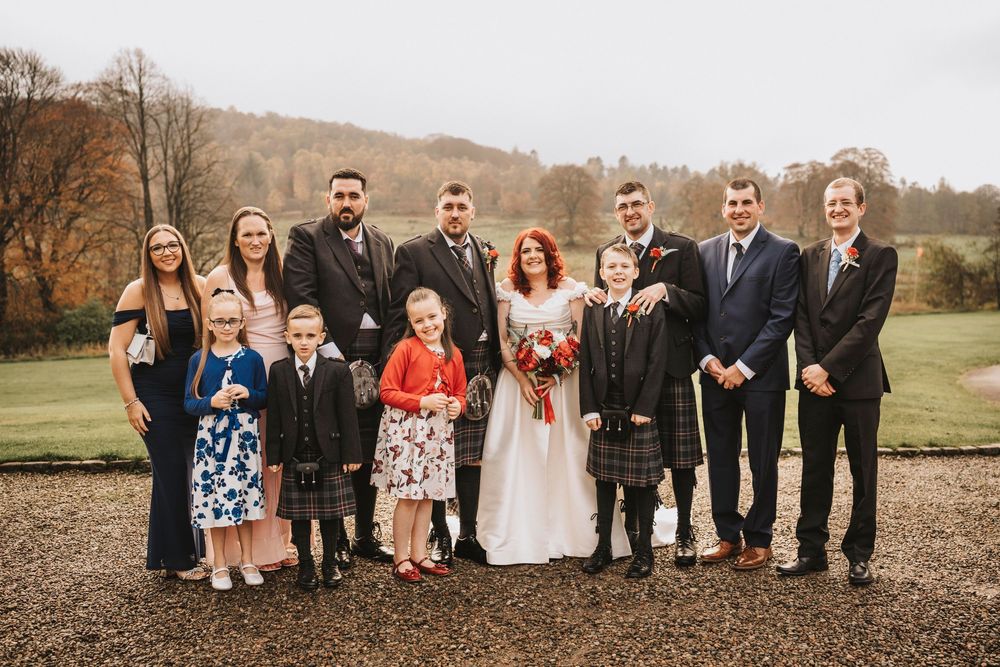 Wedding party group photo with bridesmaids and groomsmen lined up outdoors in autumn.