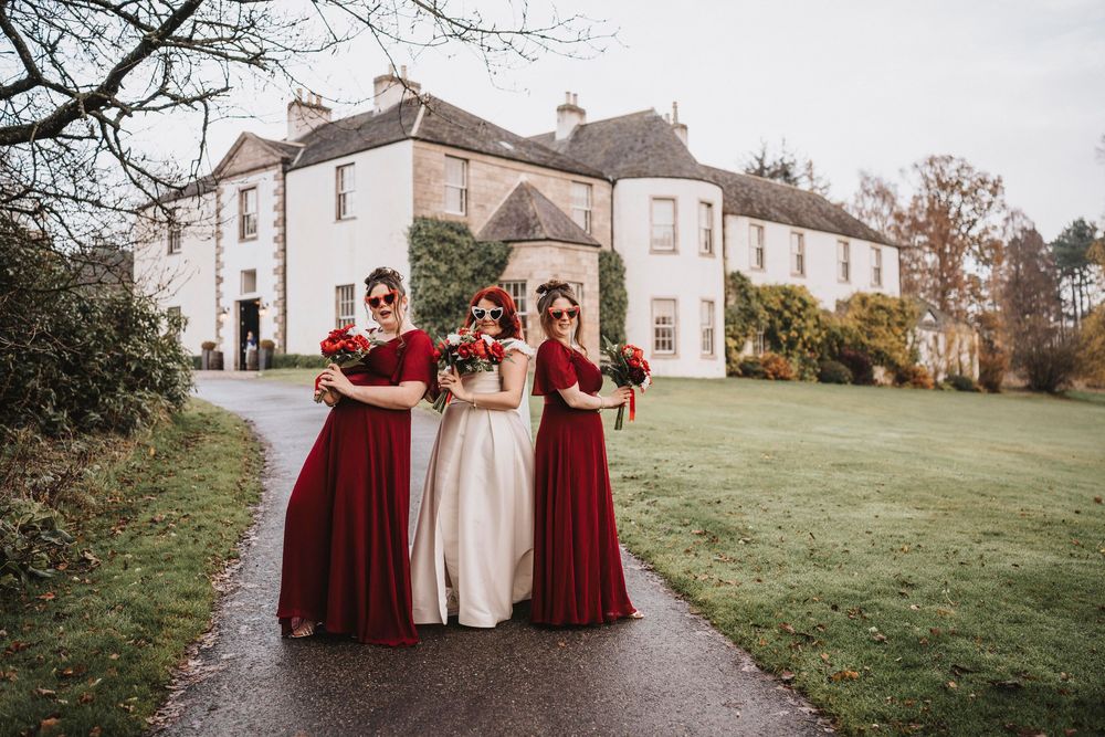 Scenic winter wedding photos captured at an elegant estate with bare trees and white buildings in the background.
