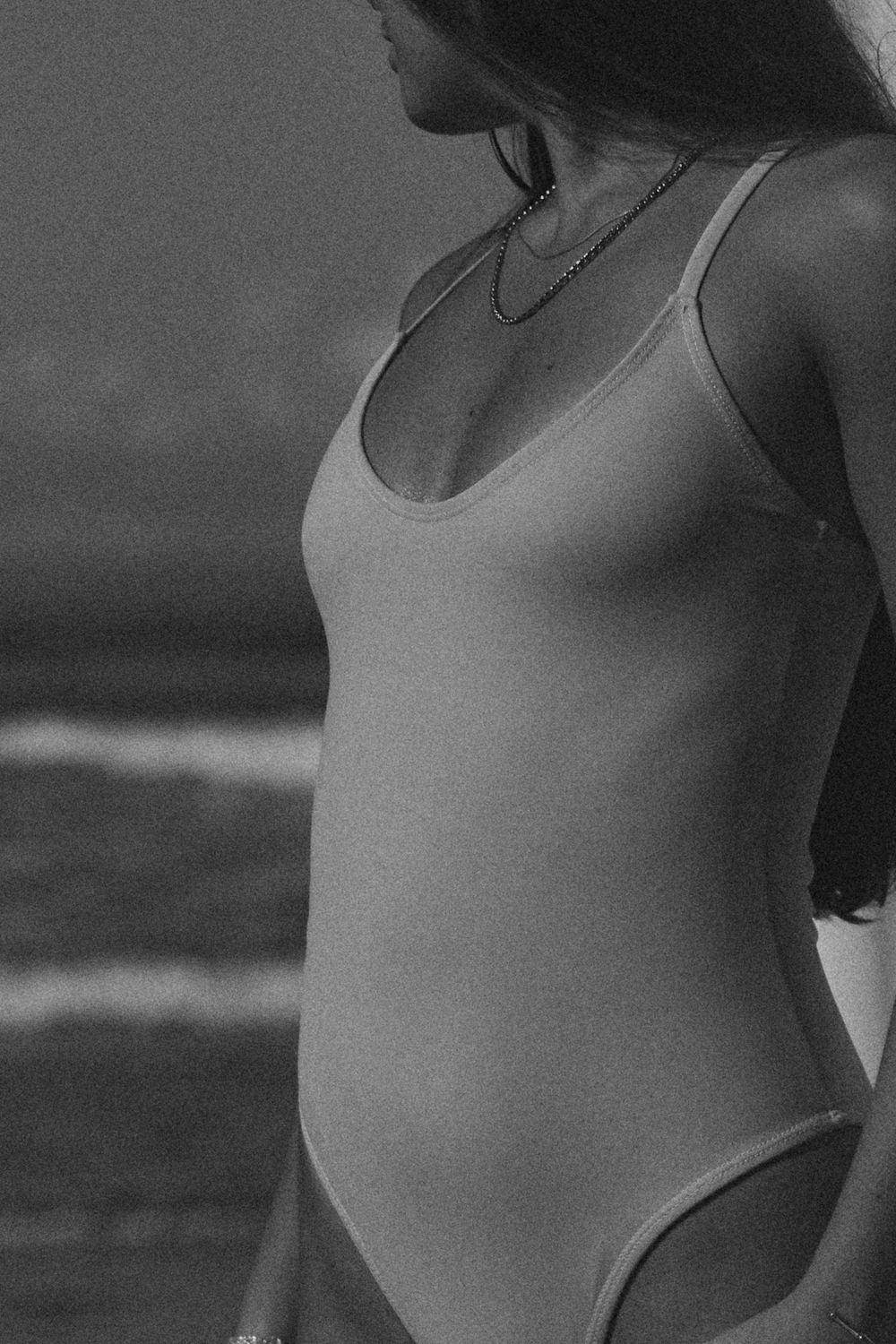 A women in a swimsuit posing against a light background at the beach during a photoshoot by photographer Rachael Kershaw.