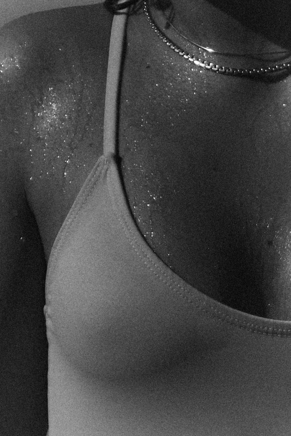 A close-up black and white photo shows a necklace against skin with soft lighting and delicate details.