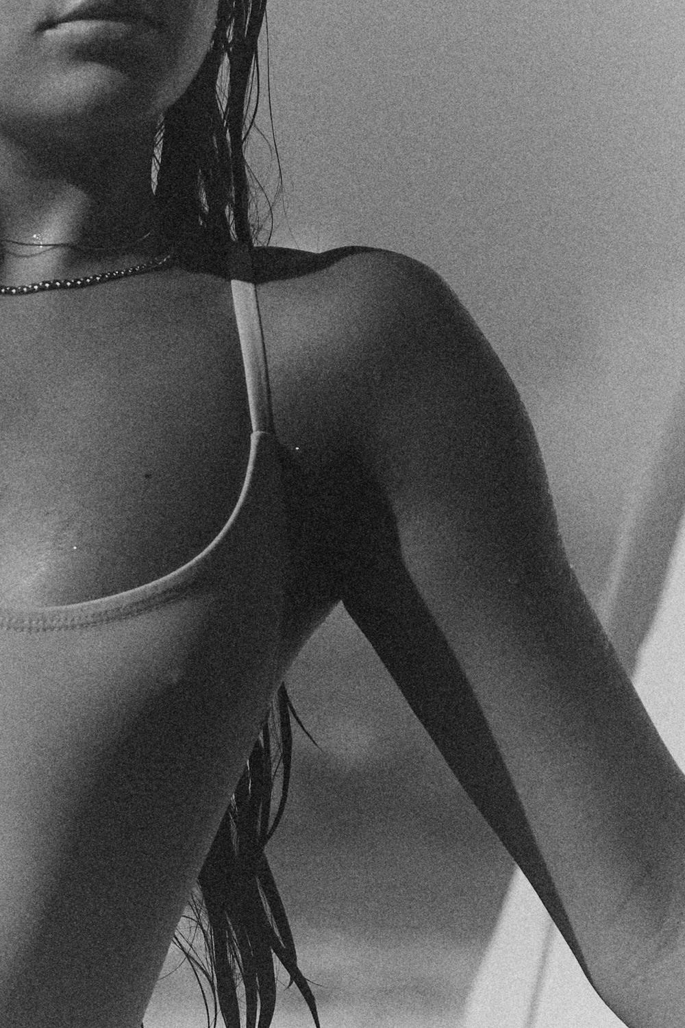 Artistic black and white close-up portrait showing shoulders with long hair and a chain necklace in dramatic lighting.