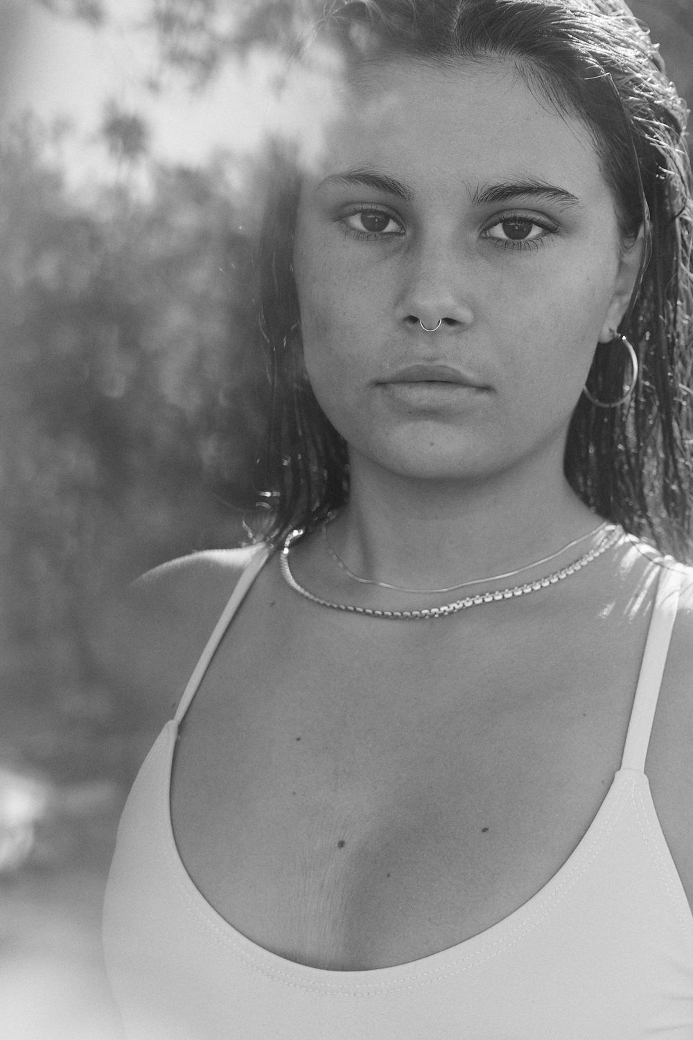 Black and white portrait series showing close-up views of a person wearing a white tank top against a blurred background.
