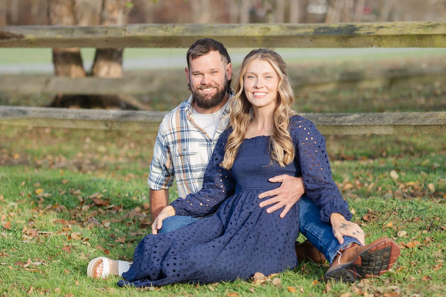 Couple sitting on autumn fall grass with pumpkins in a casual outdoor photo session.