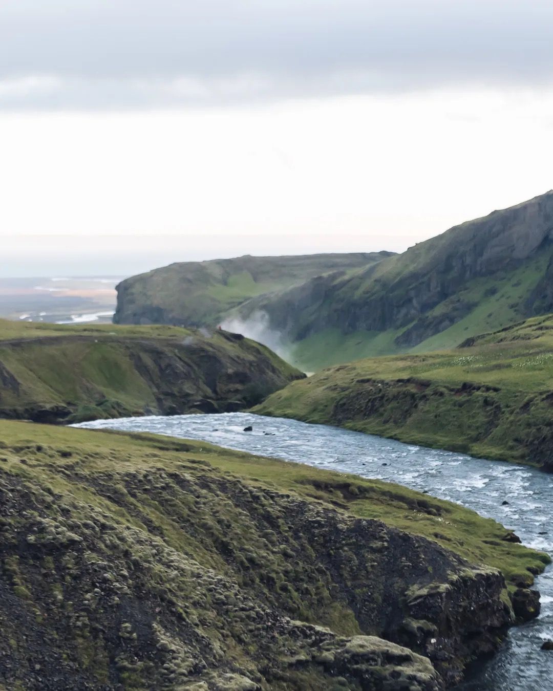 Winding river flowing through a green Icelandic valley under soft cloudy light.