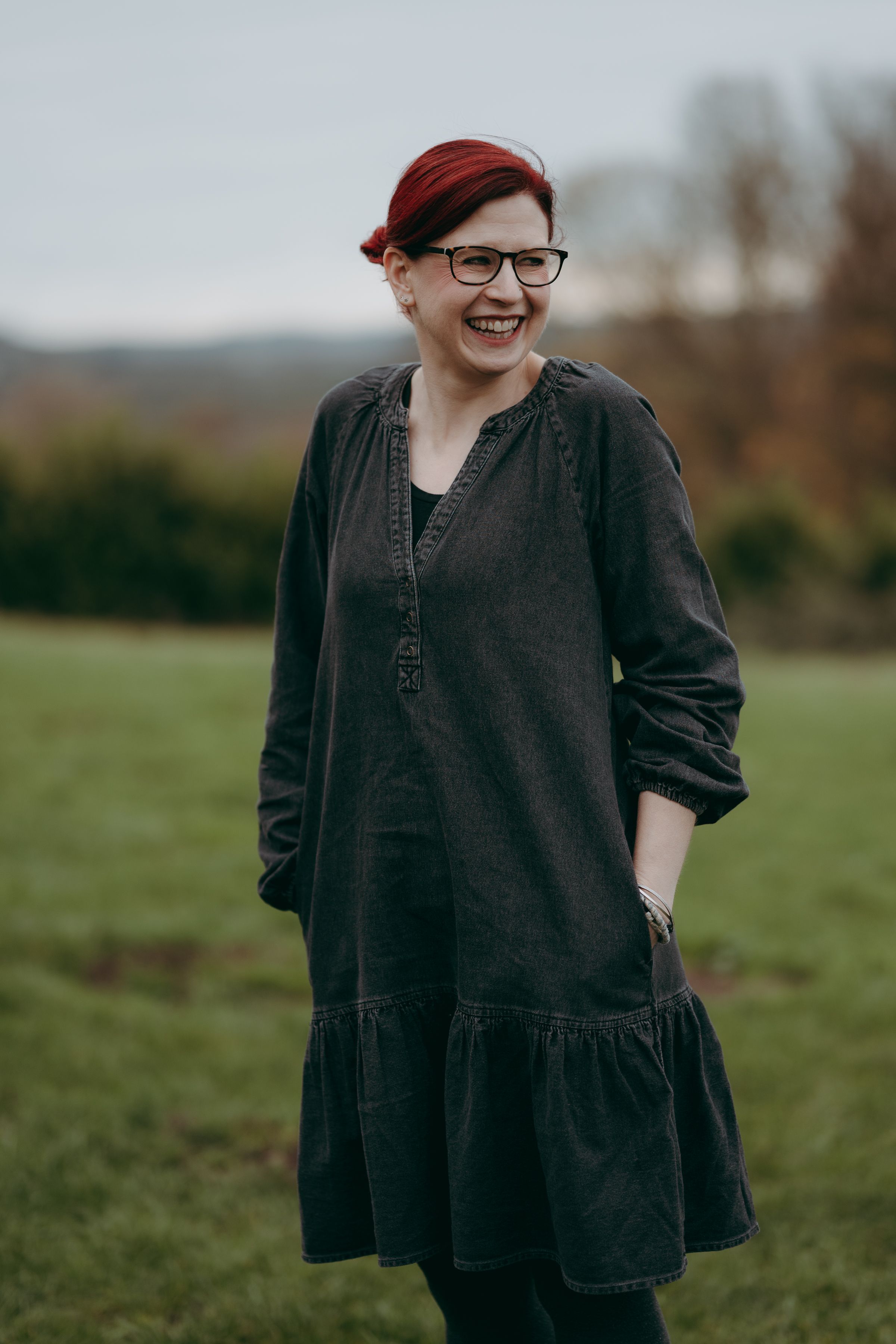 Person wearing a dark dress and red beret stands in a grassy field on an overcast day.