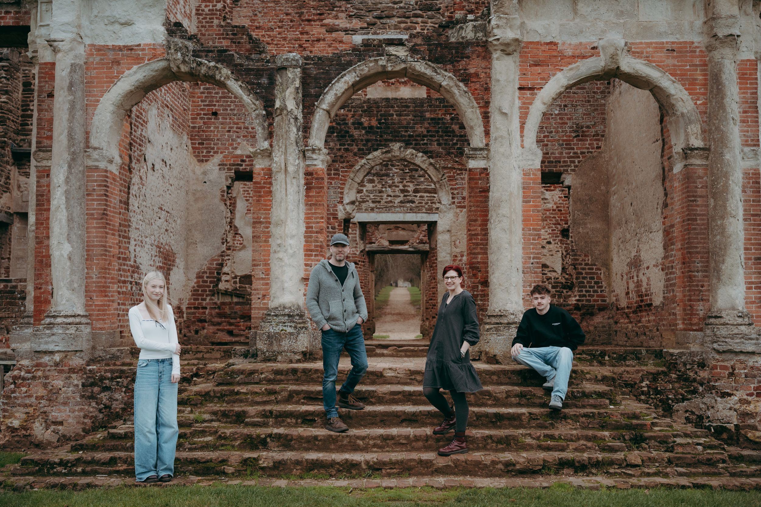People stand against weathered brick ruins of an old architectural structure with arched doorways and columns.