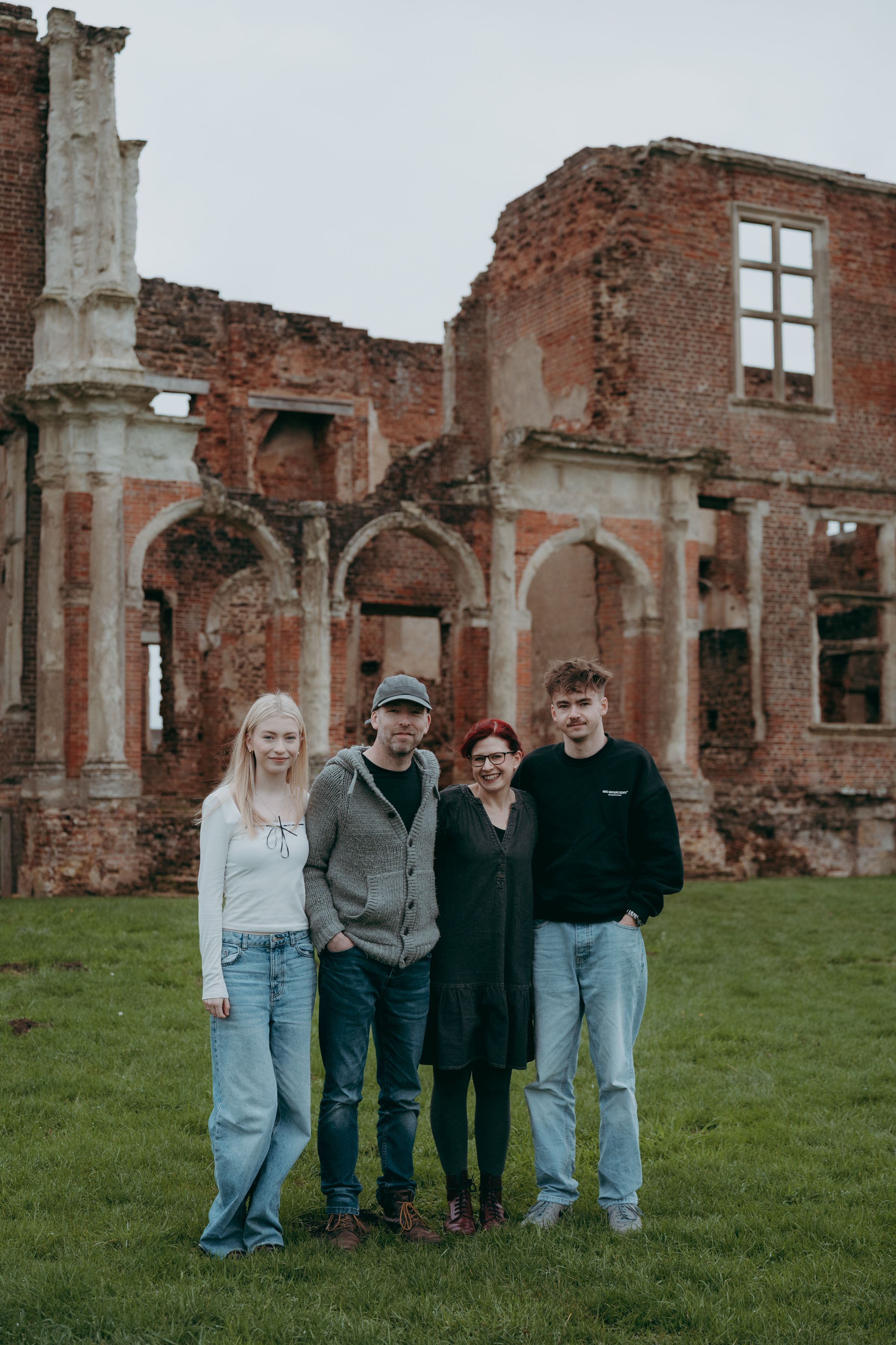 A group stands together on grassy grounds in front of old brick ruins on an overcast day.