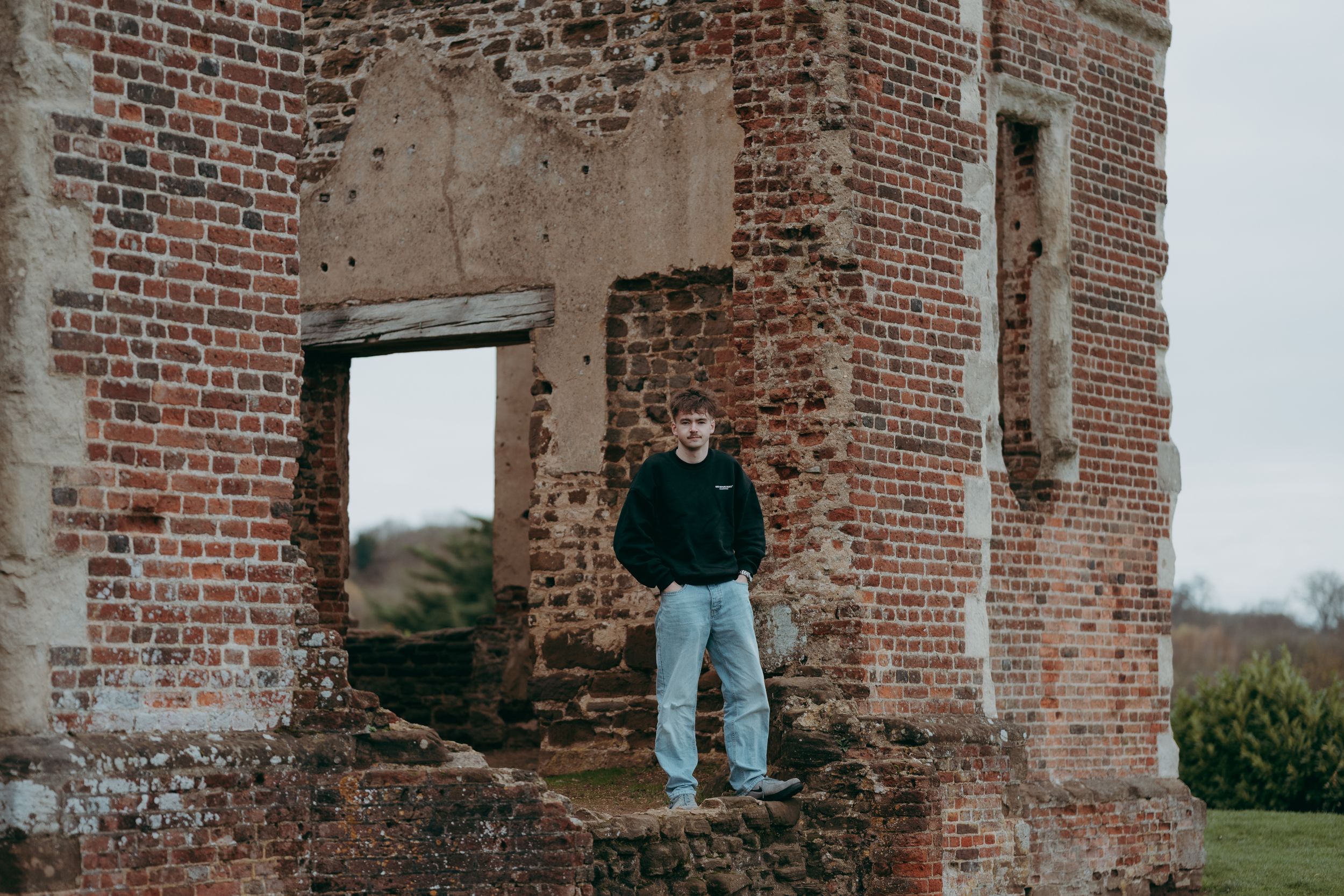 A figure sits atop a crumbling red brick wall structure in an outdoor setting.