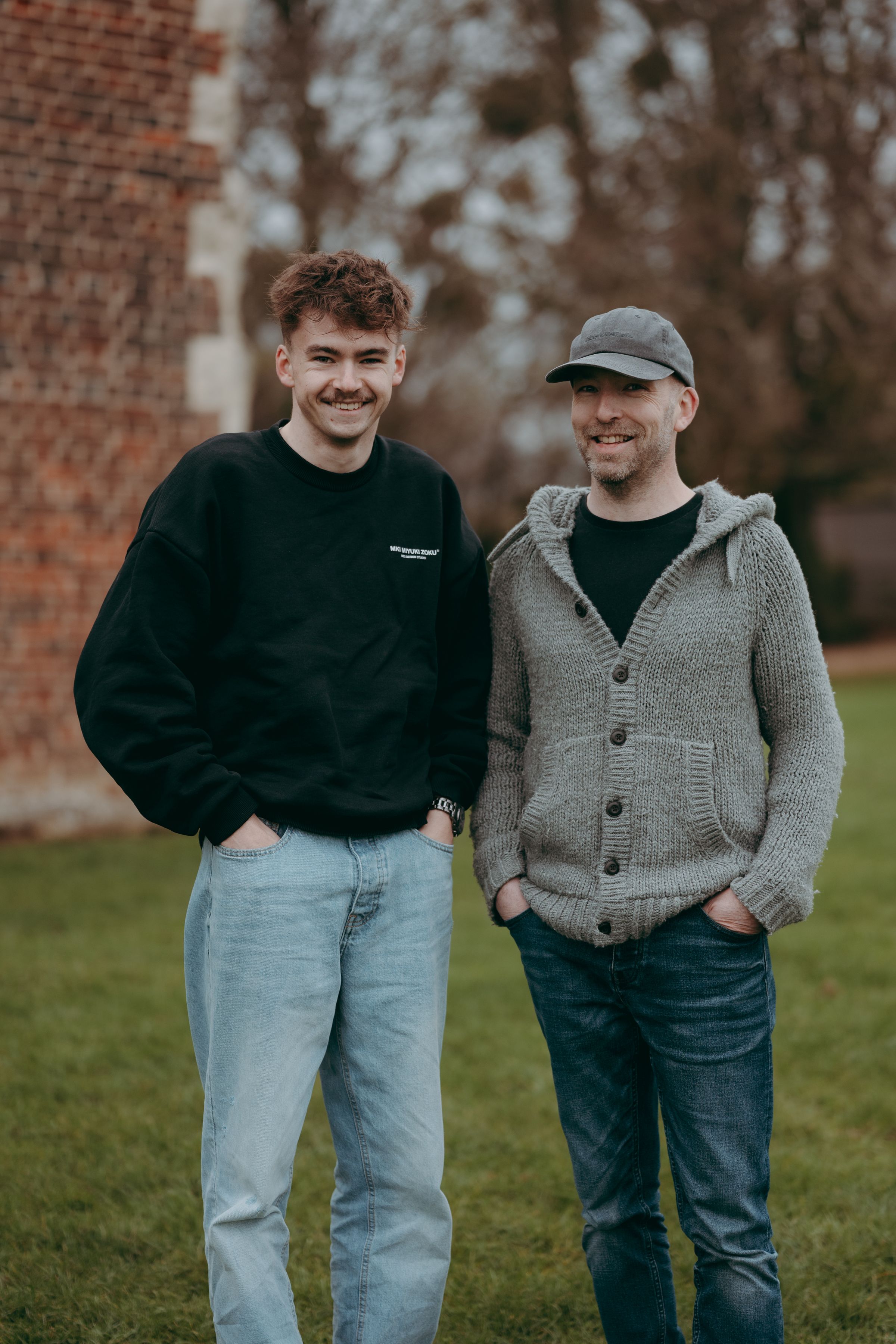 Two people in casual wear walking and smiling together against a brick wall background in natural lighting.