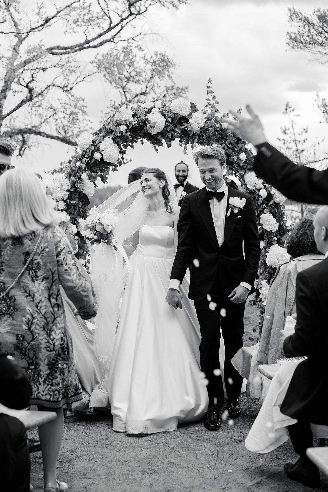 Wedding guests shower the newlyweds with confetti as they celebrate during an outdoor garden ceremony.
