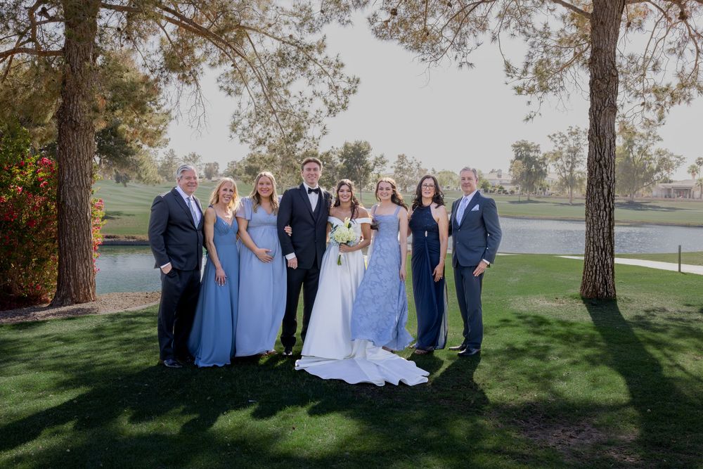 Wedding party posing on golf course lawn with bride in white gown and bridesmaids in dusty blue dresses.