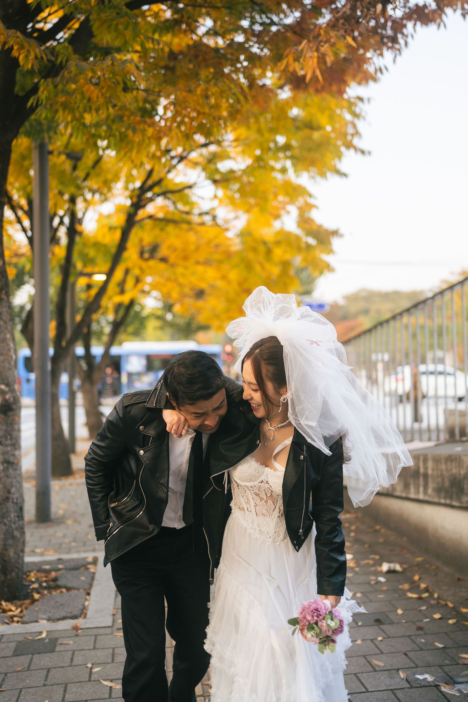 A couple shares romantic moments under golden autumn trees along a paved walkway during a fall wedding photoshoot.