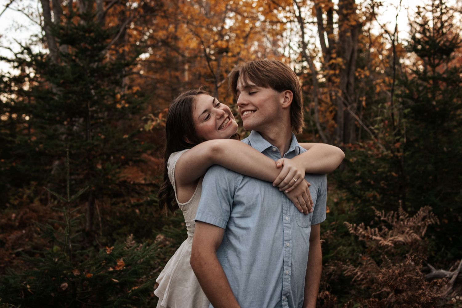 A romantic couple embraces in an autumn forest with warm golden light filtering through the trees.