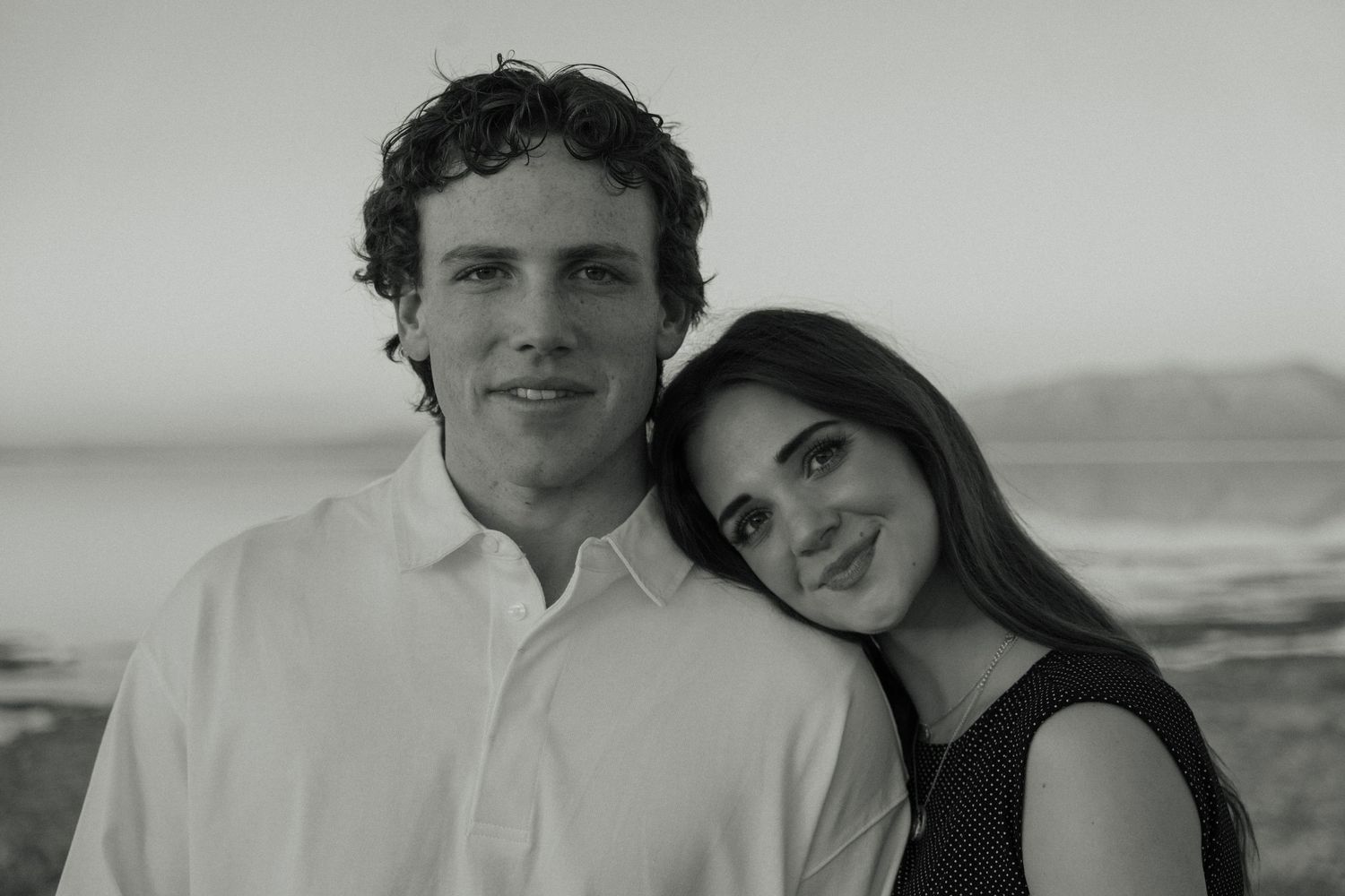 A black and white portrait of a couple posing together at the beach with a soft, blurred background.