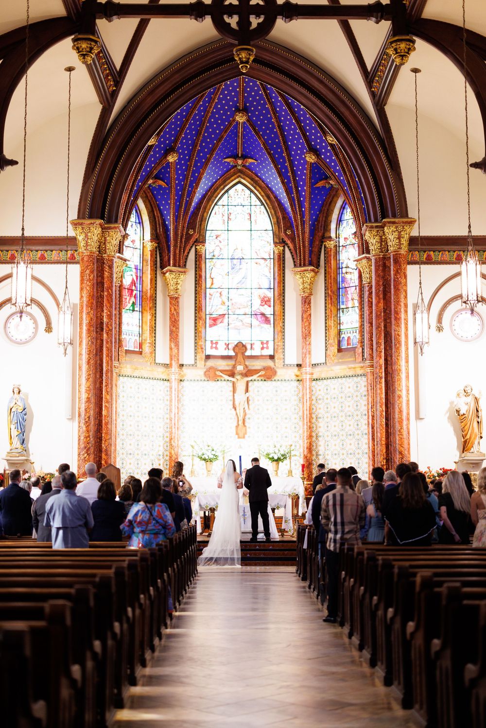 A cathedral wedding ceremony with stunning blue vaulted ceiling and stained glass windows.