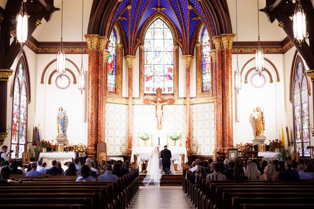 Sun streams through stained glass windows during wedding ceremony in historic church sanctuary.